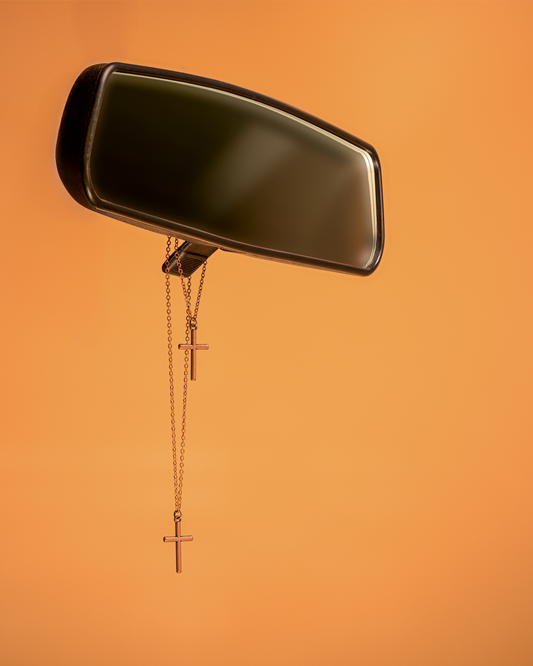 Car interior mirror with two copper cross necklaces hanging on an orange background